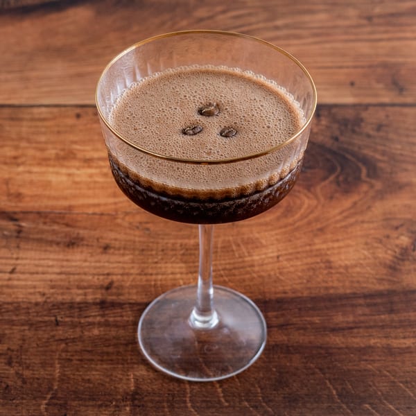 Espresso martini in a coupe glass with a gold rim, garnished with three coffee beans.