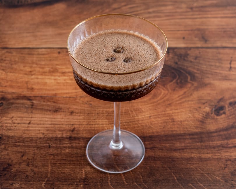 Espresso martini in a coupe glass with a gold rim, garnished with three coffee beans.