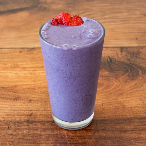 A tall glass of purple berry smoothie, topped with sliced strawberries, on a wooden table.