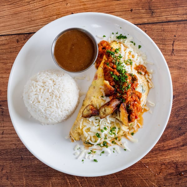 A white plate with an omelet topped with sauce, cheese, and plantains, served with rice and gravy.